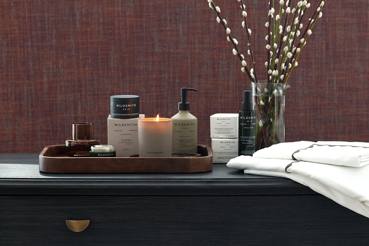 Luxury Wildsmith bathroom and skin products, lit candle and Reed Family Linen pillow cases and duvet cover set on top of a dark wooden chest of drawers - The Sleep Well Collection Giveaway Bundles with Wildsmith Skin and Reed Family Linen 